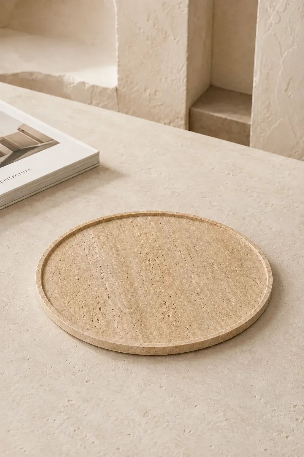 Round travertine tray displayed on a warm stone surface in a minimal architectural interior.
