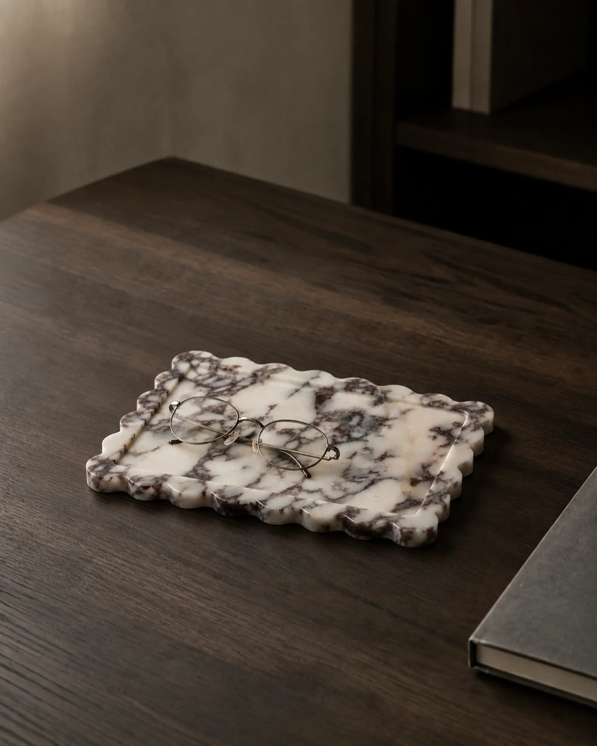 Calacatta Viola scalloped marble tray with glasses on a dark wood reading desk