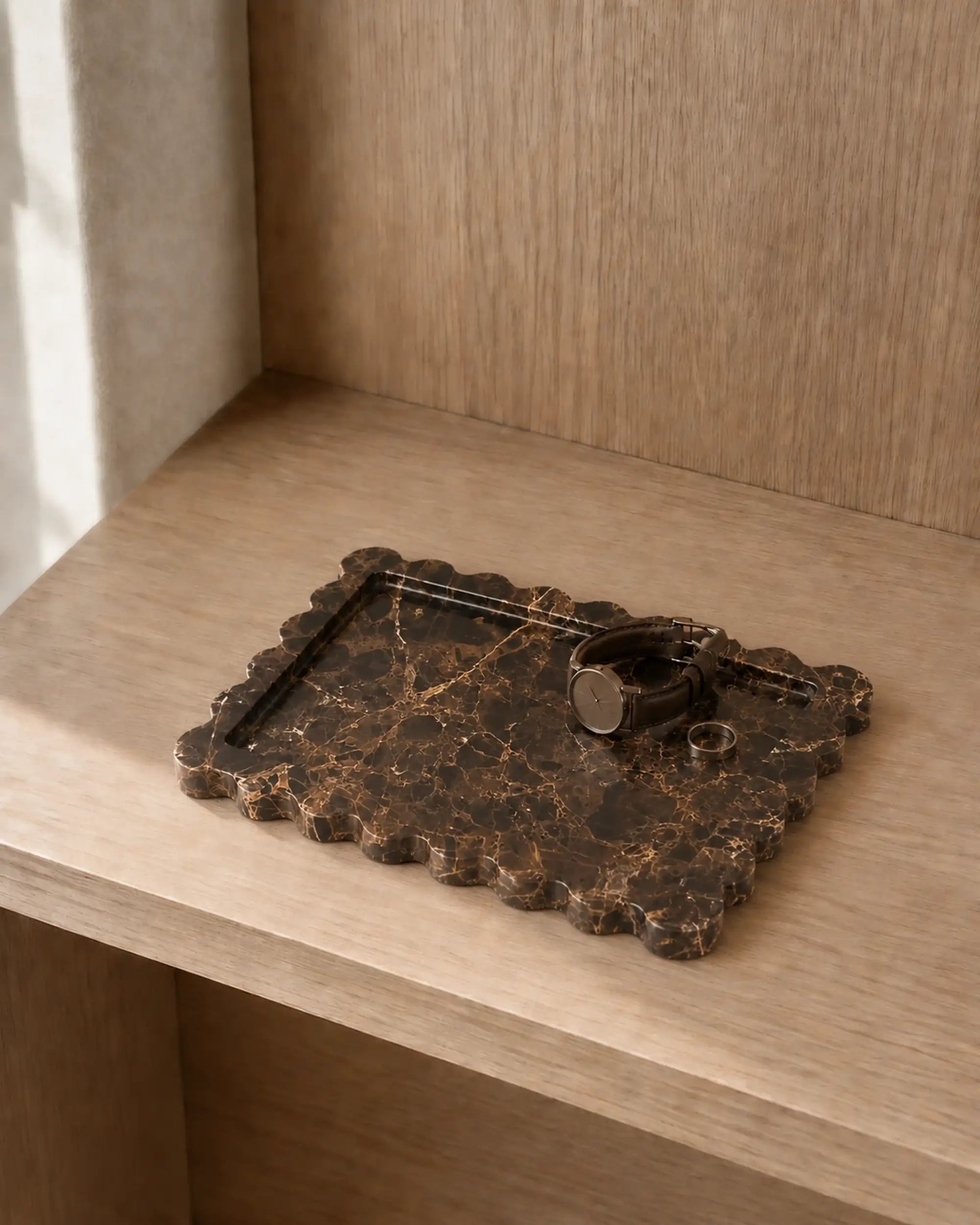 Dark chocolate brown scalloped marble tray holding a watch and ring on a light wood shelf