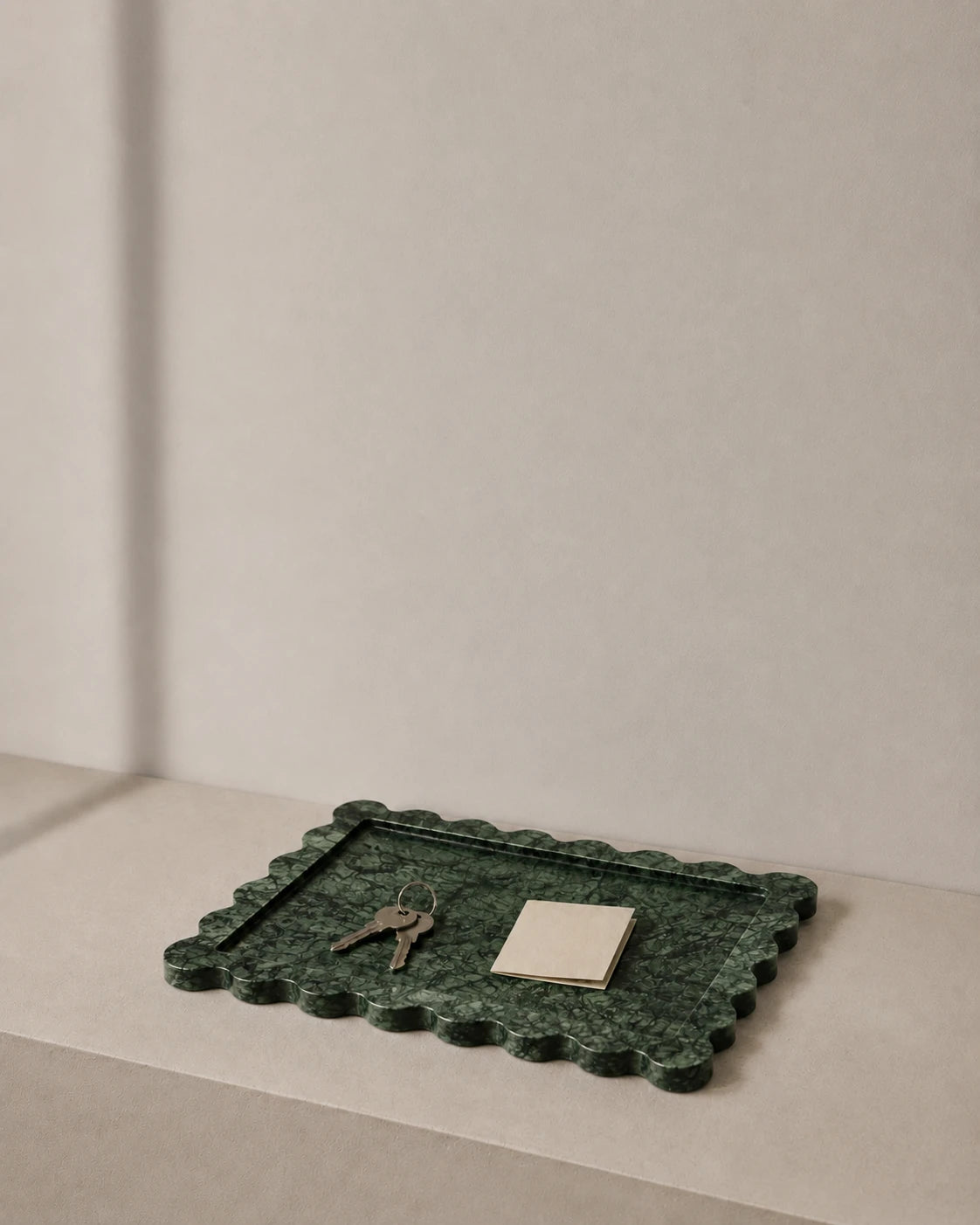 Dark green scalloped marble tray holding keys and a note on a quiet entryway shelf