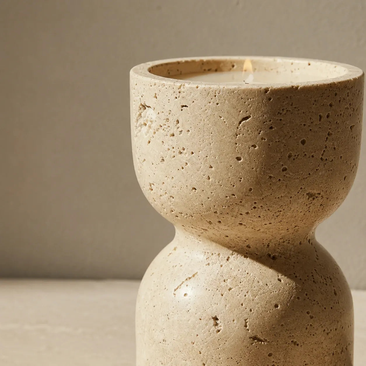 Close-up detail of a travertine hourglass candle holder showing its natural porous stone texture and sculptural waist