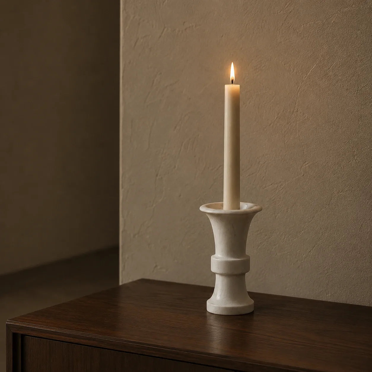 White natural marble flared candle holder with a lit ivory taper candle on a dark walnut console, showing its sculptural trumpet shape, polished finish, and subtle grey veining in warm evening light.