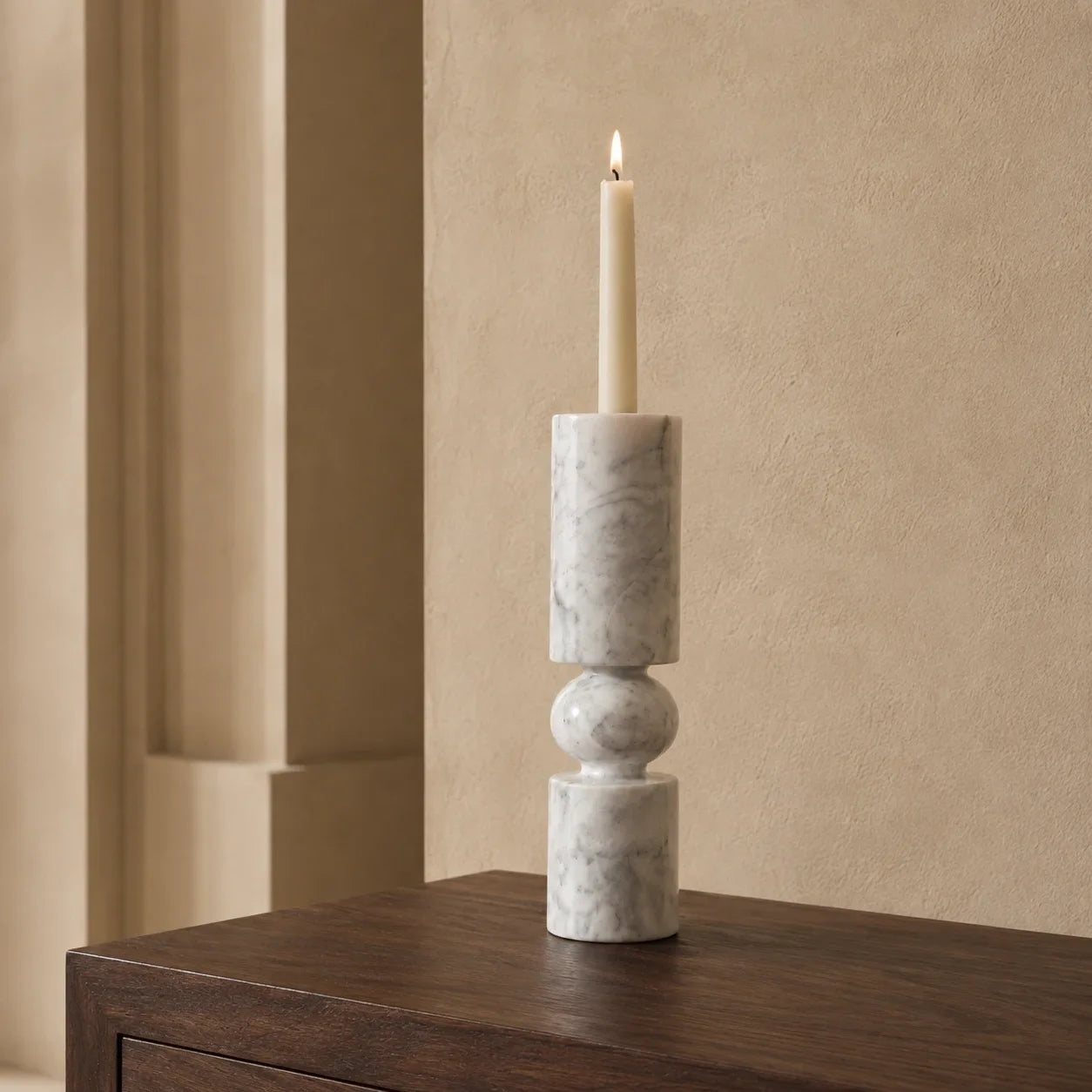 White natural marble pillar candle holder with a sculptural stacked design, rounded stone sphere detail, and grey veining displayed on a walnut table in a warm architectural interior.