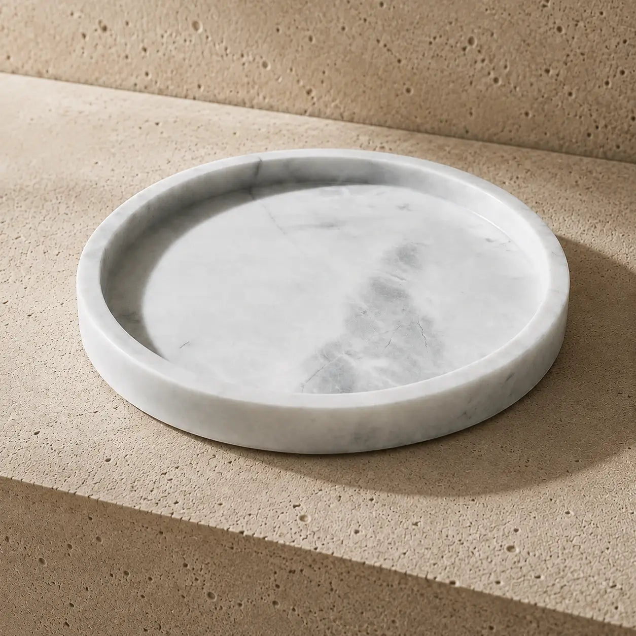 White natural marble round tray with a shallow carved surface and polished rounded edge, displayed on a limestone surface to highlight its subtle grey veining, stone texture, and timeless minimalist design.