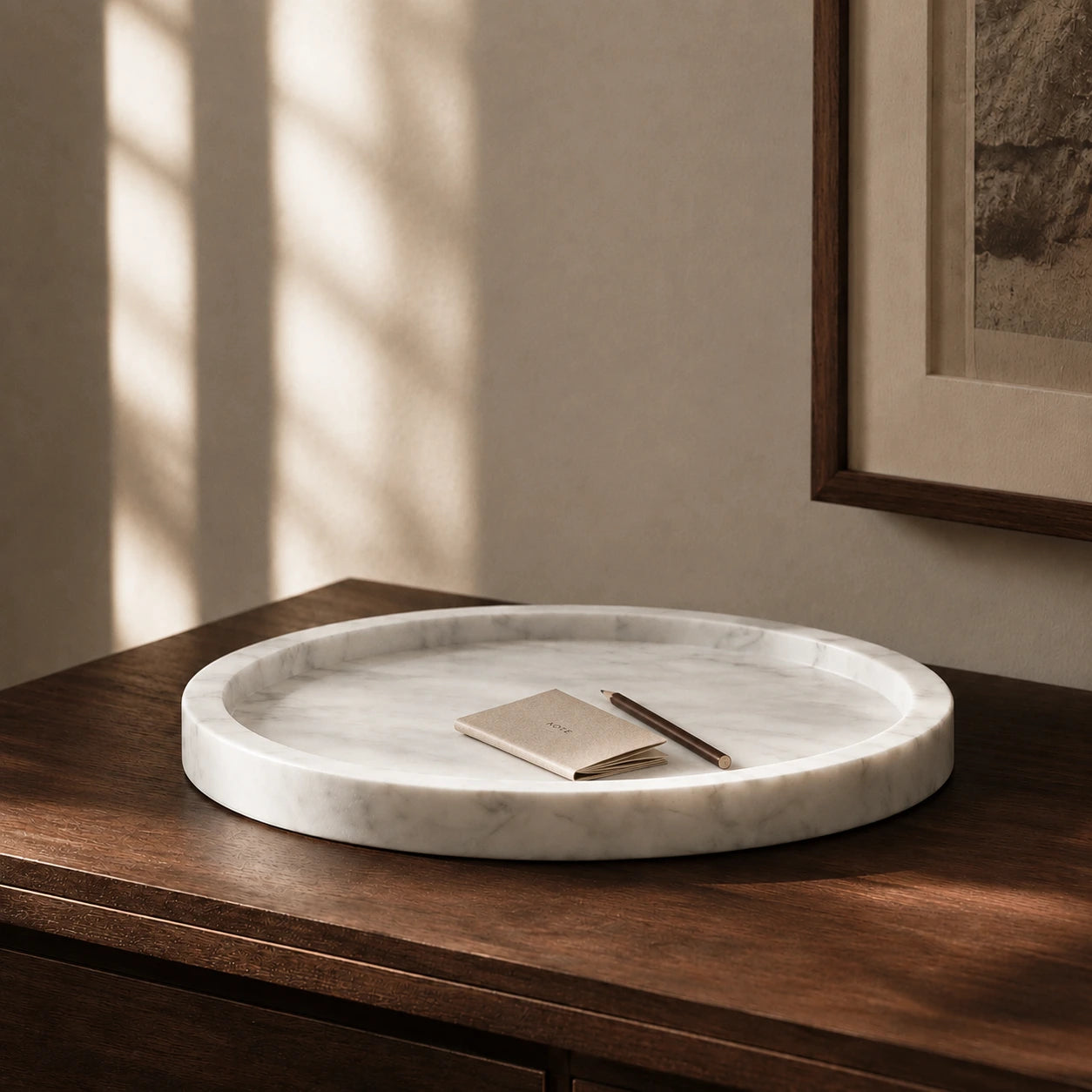 White natural marble round tray styled with a notebook and pencil on a walnut surface, showcasing its thick rounded edge, shallow carved design, subtle grey veining, and timeless stone craftsmanship.