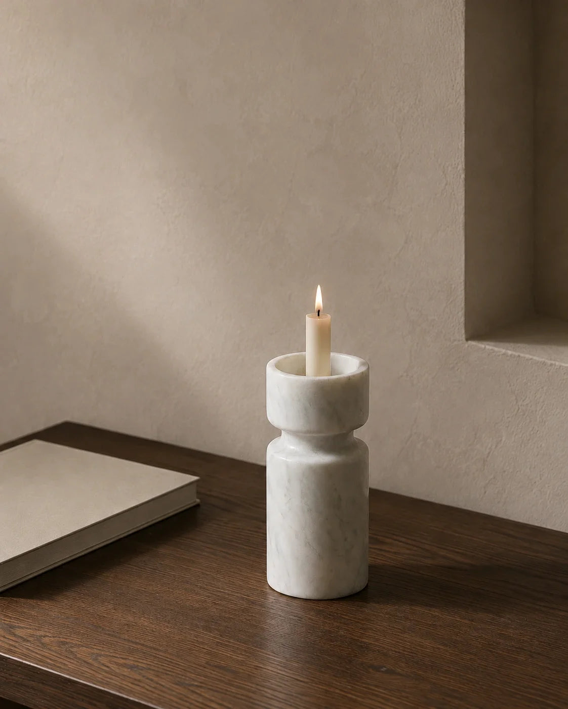 White marble sculptural candle holder with ivory taper candle on a dark wood table